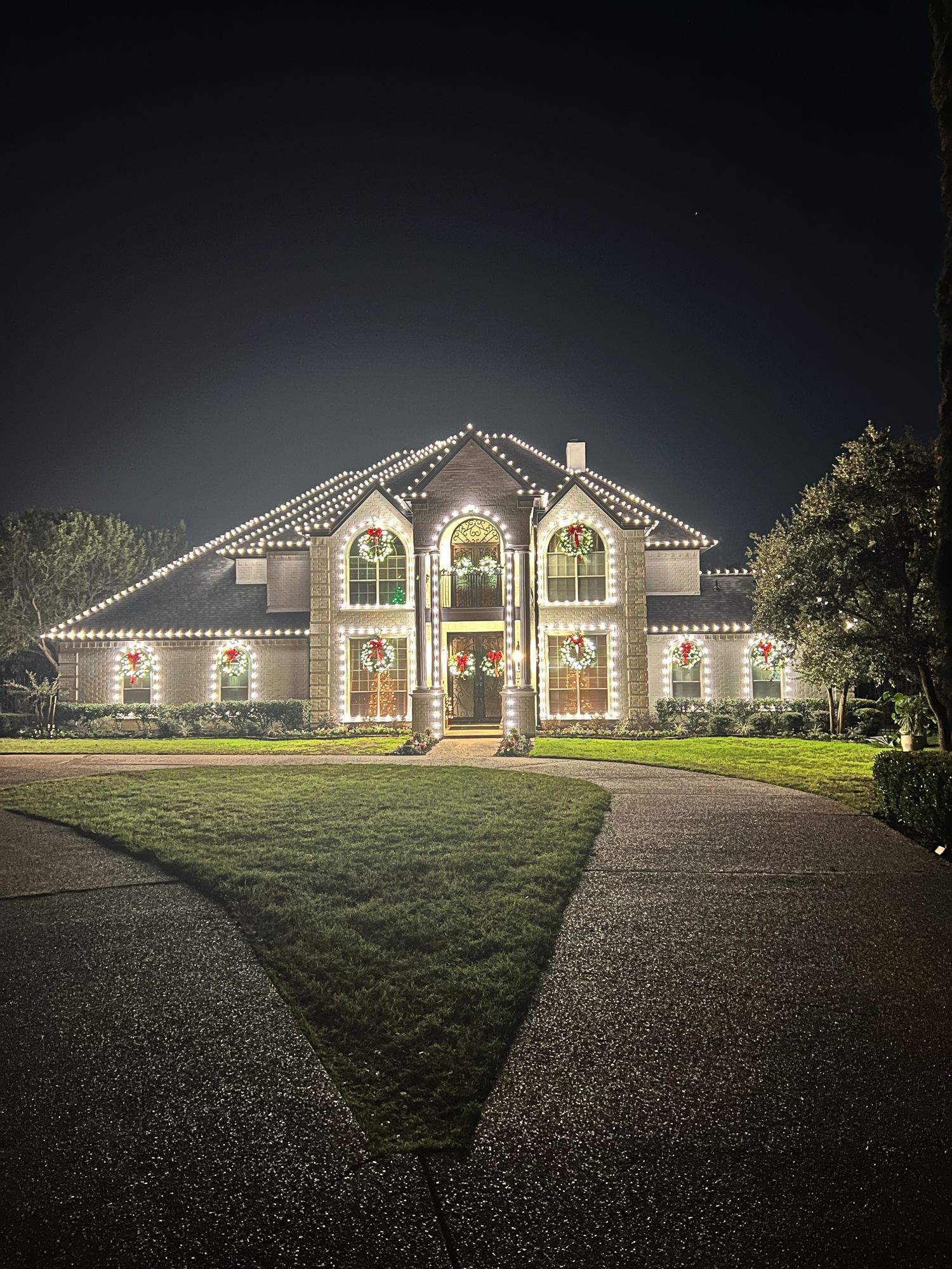 Two-story home outlined in warm white Christmas lights with wreaths in every window, installed by Corzo